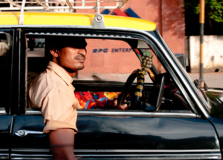 © florian grassecker taxifahrer wartet in indien in schwarz gelbem taxi, die rechte hand haengt zum fenster raus