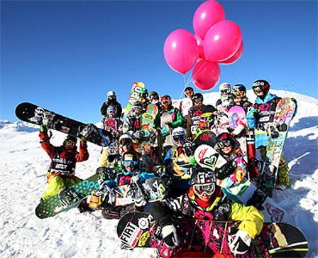 Eine Gruppe Snowboarder kniet im Schnee und hält rote Luftballons