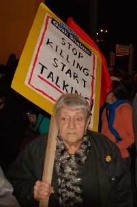 Eine Frau trägt bei einer Demonstration ein Schild mit der Aufschrift "Stop Killing Start Talking"