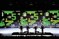 Die Band Kraftwerk vor einer großen Videoprojektion mit unterschiedlich großen, stilisierten Ziffern.