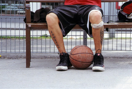 Ein Mann sitzt auf einer Bank und hält zwischen den Füßen einen Basketball