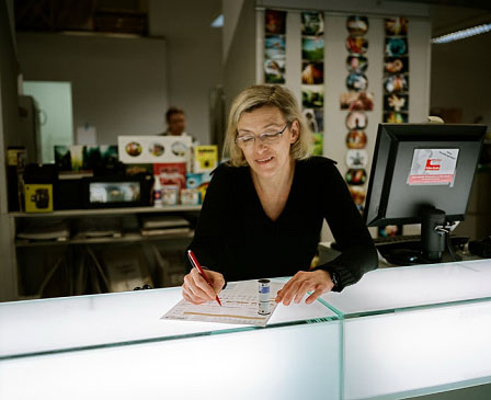 Filmentgegennahme durch eine blonde Dame mittleren Alters im Fotolabor.