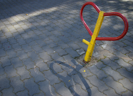 ein Ausschnitt eines Parkplatzes, mit einem metallenen klappbaren Ständer, um den Parkplatz freizuhalten. Der hat die Form eines Herzes.