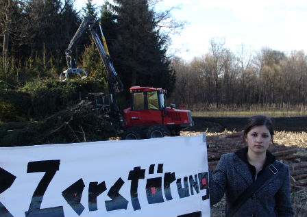 frau mit demo-transparent. dahinter ein traktor mit baumstämmen.