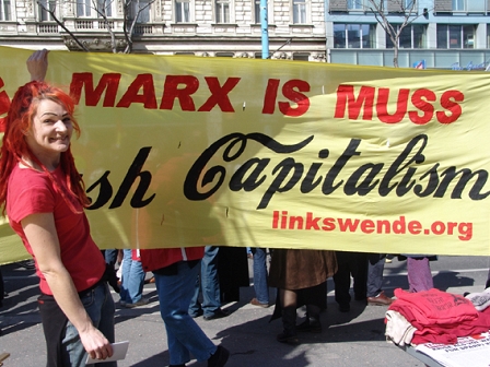 Frau hält bei einer Demo einen Banner hoch, auf dem "Marx is Muss" steht