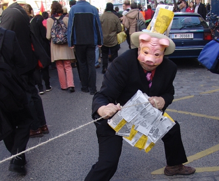 Demonstration in Wien; Mann mit Schweinemaske hält Geldkoffer in der Hand