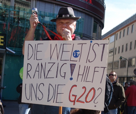 Demo in Wien, Mann hält ein Schild, auf dem "DIe Weöt ist ranzig, hilft uns die G20?" steht