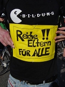 Ein schwarzes T-Shirt, mit einem Aufdruck "Reiche Eltern für alle", der sich über die gesamte Brust erstreckt.