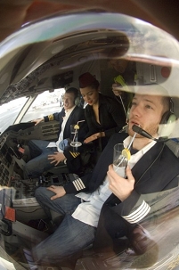 DJ Dero und Kollegen sitzen in einem Flugzeugcockpit mit Cocktails in den Händen.