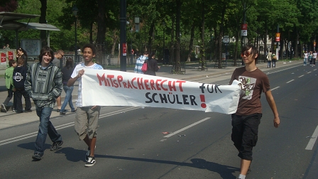 Strahlender Sonnenschein. Zwei Schüler halten ein Plakat mit der Aufschrift "Mitspracherecht für Schüler".