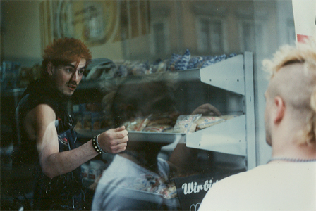 ein Punk vor einem DDR-Supermarkt, einer drinnen 