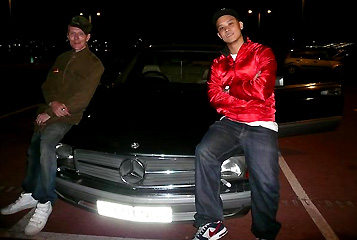 © DJ Beware Rob Birch mit DJ Beware an seiner Seite, auf der Motorhaube eines dunklen Wagens deutscher Produktion.