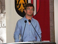 Ein Junge im gestreiften Hemd steht mit leicht mitleidigem Blick hinter einem Podium.