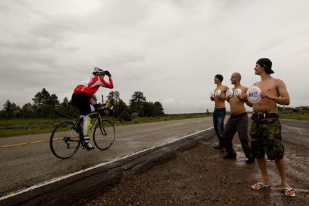 © Alexander Karelly Christoph Strasser faehrt rad, seine freunde stehen mit nacktem oberkoerper am strassenrand und halten schilder mit 1000 miles