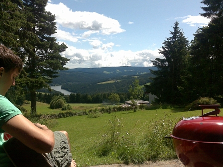 Ausblick auf einen See, umgeben von bewaldeten Hügeln.