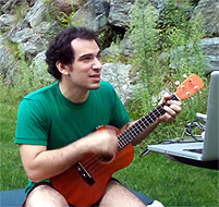 Der Sänger Jonathan Mann mit Gitarre und Laptop in einer Naturidylle.