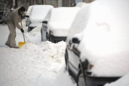 Schneeschaufelnder Mann, völlig verschneite Autos