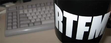 Eine Tasse, auf der "RTFM" geschrieben steht, vor einer Computertastatur.