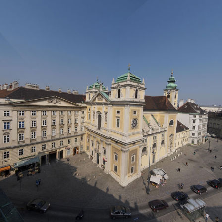 Das große Schottenstift in der Wiener Innenstadt vom gegenüberliegenden Dach aus fotografiert. Großer Platz, gelbe Kirche und viel Himmel.