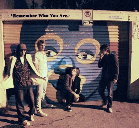 Bandmitglieder von Foster The People stehen vor Garagenwand. Remember Who You Are steht drüber.