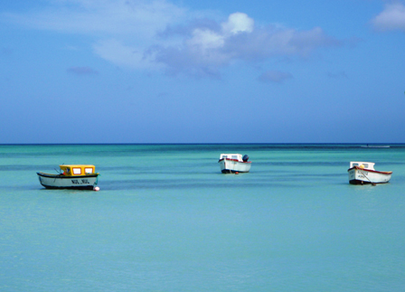 © priska bilgeri drei kleine boote im tuerkisen meer der karibik, dahinter blauer himmel