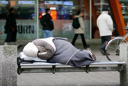 Obdachloser auf einer Bank am Gehsteig