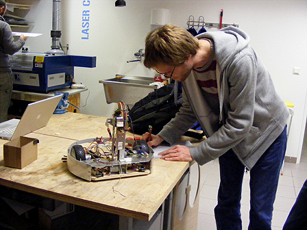 Ein junger Mann, der sich Notizen macht, daneben steht ein Roboter mit zwei Rädern.