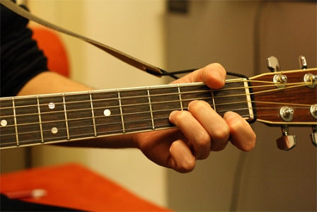 Hand, die Akkord auf einer Gitarre greift