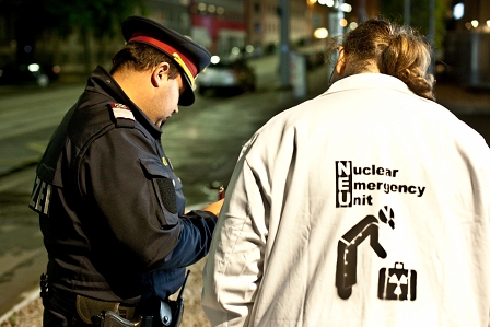 polizist schreib einen spialteilnehmer mit "nuclear emergency unit"-jacke auf.