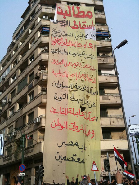 Hochhaus mit Riesentransparent in arabischer Schrift mit den Forderungen der Bewegung