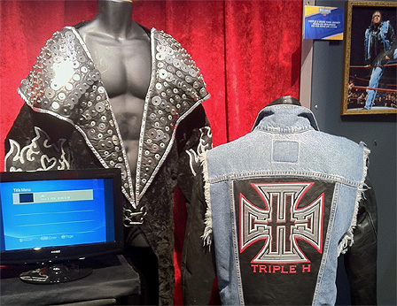© Maciej Palucki Ein Mantel mit großem Ausschnitt und einem großen, Nieten besetzten Kragen. Daneben eine hellblaue Jeansjacke von hinten fotografiert, mit einem schwarzen "Triple H"-Segment in Leder.