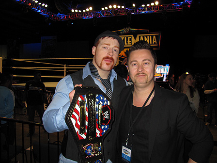 © Heiko Link Maciej Palucki mit dem Wrestling-Star Sheamus, der einen großen Gürtel in der Hand hält, der mit der "Stars & Stripes"-Flagge der USA und goldbesetzten Plaketten verziert ist.