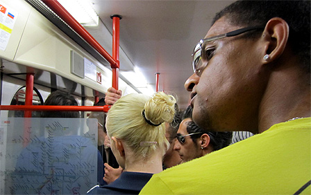 Eine blonde Frau von hinten und ein Mann mit Sonnenbrille und gelbem Shirt im Vordergrund, der gerade nach links sieht.