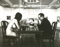 Marcel Duchamp spielt mit einer nackten jungen Frau eine Partie Schach, dahinter steht Duchamps Kunstwerk "Großes Glas".