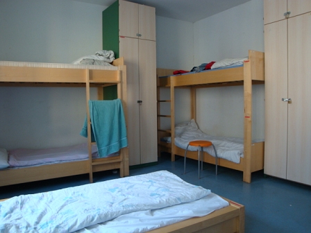 Notquartier im JuCa; ein Einzelbett und zwei Stockbetten, dazwischen Kästen, Handtücher etc.