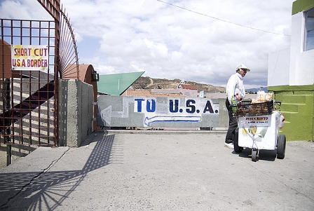 Betonterasse mit Aufschrift to U.S.A. Daneben ein Schild mit der Aufschrift Shurt Cut USA Border. Am RAnd ein Alter Mann mit Einkaufswagen