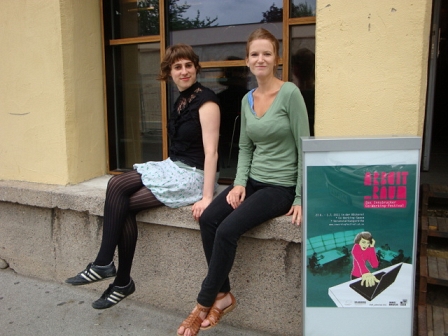 Zwei Frauen auf einem Fenstersims neben einem Plakat