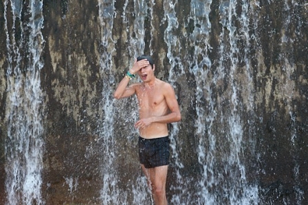 Mann mit Festivalband in Badehose vor Wasserfall.