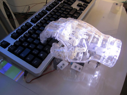 Eine weiße, transparente und beleuchtete Roboterhand, die auf eine Computertastatur tippt.