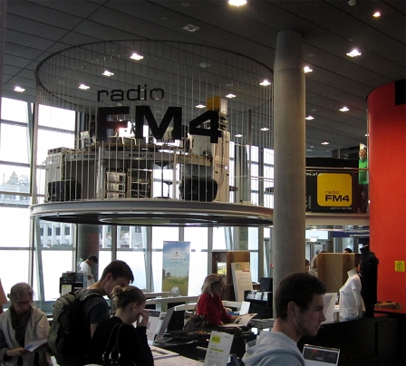 Der Empfangsbereich des Ars Electronica Center, darüber ein runder, von der Decke hängender Balkon. Darin befindet sich das mobile FM4 Studio.