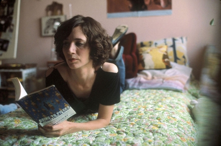 Miranda July auf einem Bett liegend und lesend