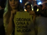 Junge Frau hält ihre Stofftasche mit der Aufschrift "George, Gina und deine Mudda" hoch