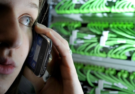 angeschnittenes Gesicht, eine Hand hält ein Handy ans Ohr im Hintergrund sieht man grüne Kabel