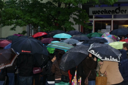 Menschen mit Schrimen im Regen, drängen auf Tür zu.