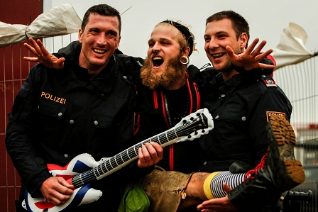 Ein Punk spielt Luftgitarre mit zwei Polizisten am Nova Rock