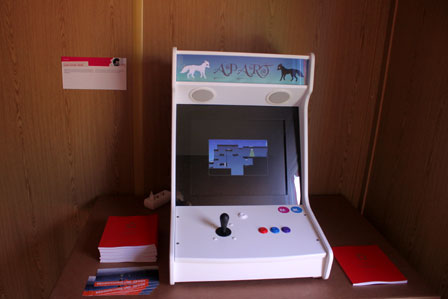 Ein weißer Videospielautomat mit Joystick und bunten Knöpfen, auf dem das Spiel "Apart" läuft.