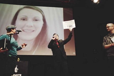 Susanne Posegga gewinnt den Elevate Artivism Award und ist via Videochat zugeschalten. Hermes hält einen Zettel mit dem darauf notierten Geldpreis in die Luft.