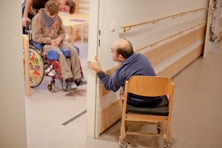 Mensch schaut in ein Zimmer mit einer Person im Rollstuhl