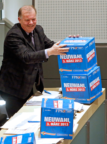 Kärntner Landtagsabgeordneter mit Schachteln mit der Aufschrift "Neuwahl 3. März 2013"