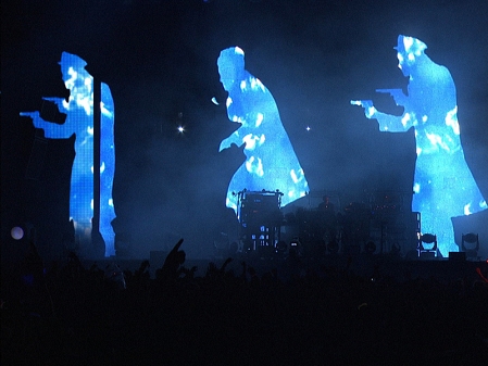 Bühne mit Visuals: Drei Lichtgestalten, die wie Kommissare und ein Verfolgter aussehen